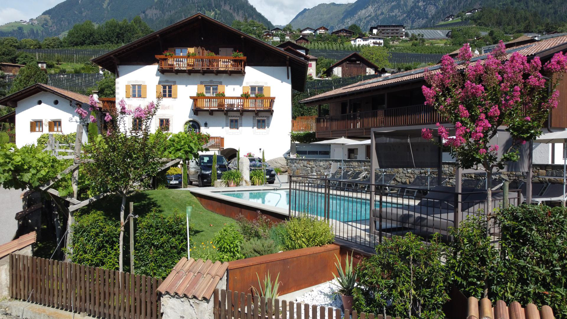 Sommerliche Gesamtansicht des Mayerhofs in Kuens bei Meran mit Salzwasserpool, üppigem Garten und Blick auf die umliegenden Südtiroler Berge