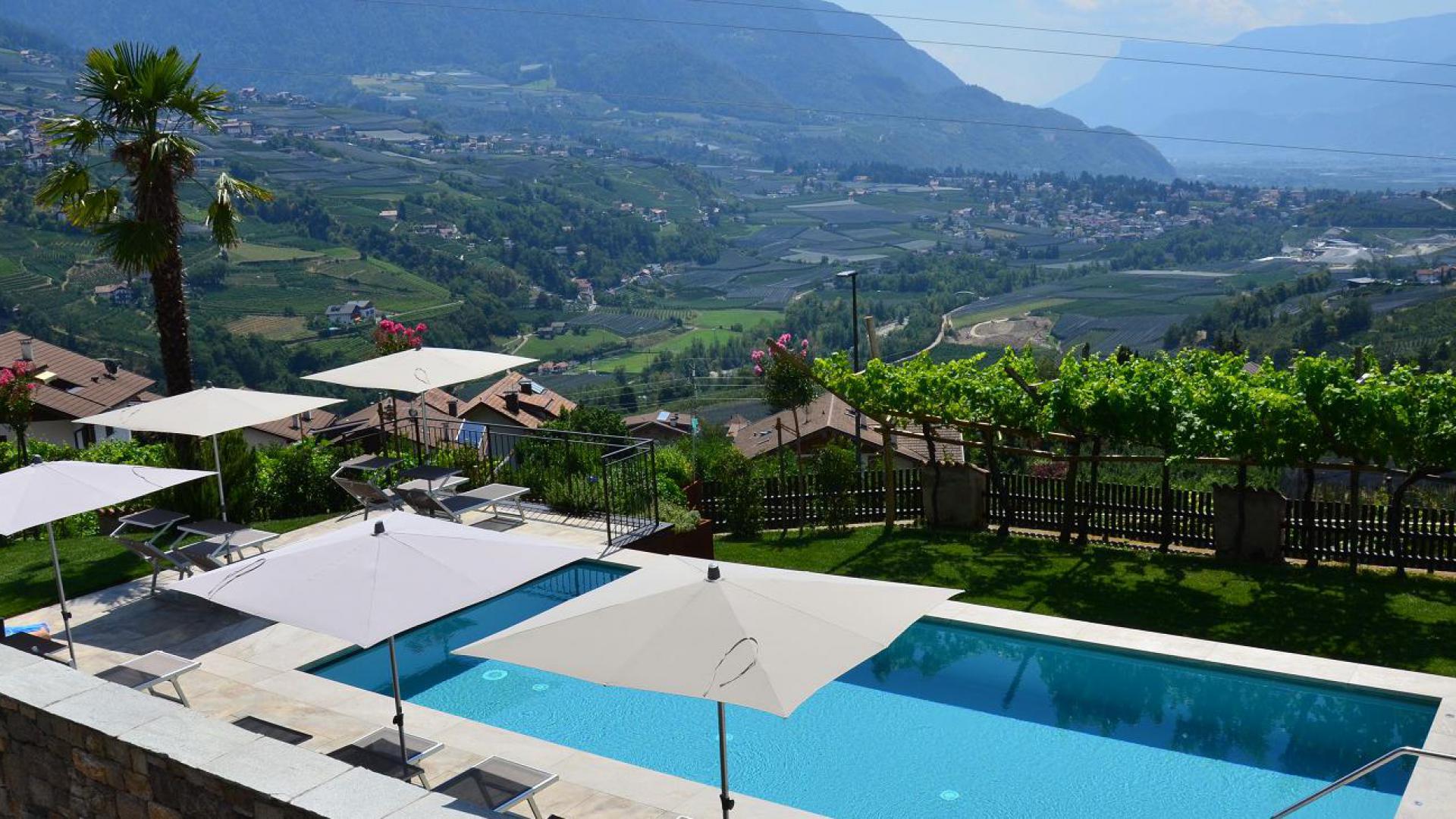 Weitläufige Poolanlage mit Liegewiese und Sonnensegeln am Mayerhof in Kuens – Blick über Weinberge und Obstgärten ins Meraner Becken und Etschtal